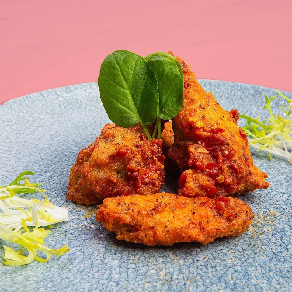 Crispy Asian-fusion chicken wings with chili flakes and spinach on a blue plate.