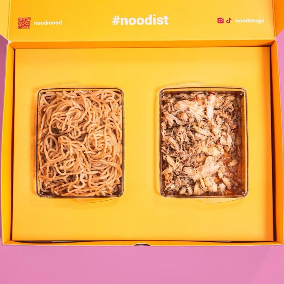 An open Noods To Go box with two containers: one with noodles, the other with shredded chicken.