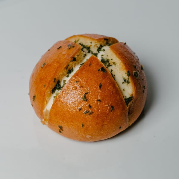 A golden-brown Korean cream cheese garlic bread, cut into quarters and filled with creamy white cheese and herbs.