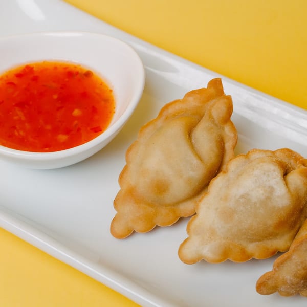Golden-fried dumplings with a side of vibrant red chili sauce on a white rectangular plate.