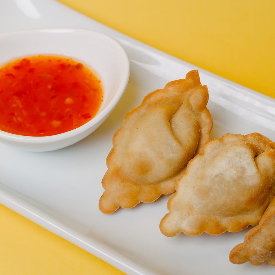 Golden-fried dumplings with a side of vibrant red chili sauce on a white rectangular plate.