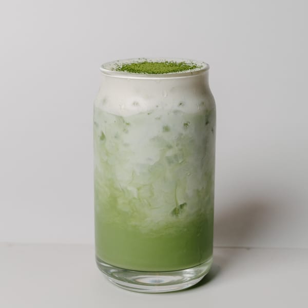 Iced matcha latte with a thick layer of foam and green powder on top, in a clear glass.