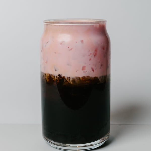 A glass of Noods To Go's dark iced coffee topped with a thick layer of pink foam.