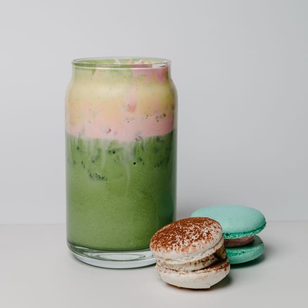 A colorful layered drink with green, pink, and yellow, next to two macarons.