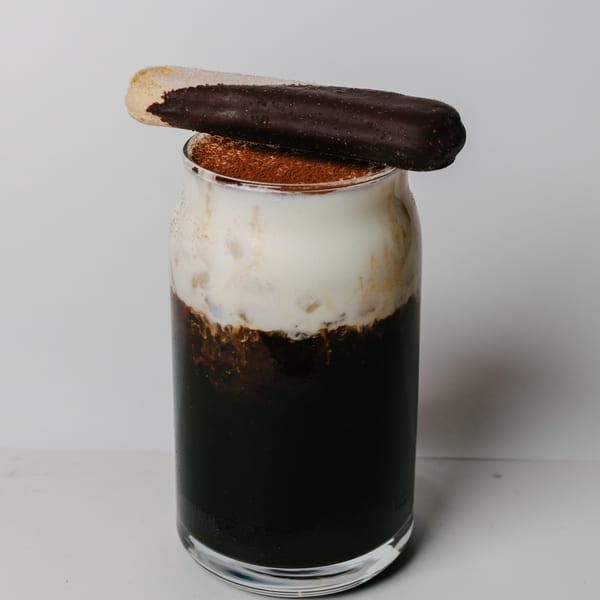 A dark drink with white foam and cocoa powder, topped with a chocolate-dipped cookie.