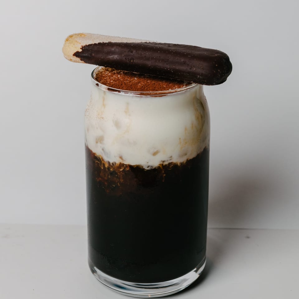 A dark drink with white foam and cocoa powder, topped with a chocolate-dipped cookie.