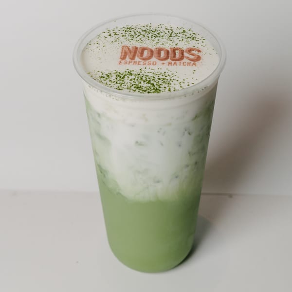 Noods To Go matcha latte with cream, topped with matcha powder and the Noods logo.