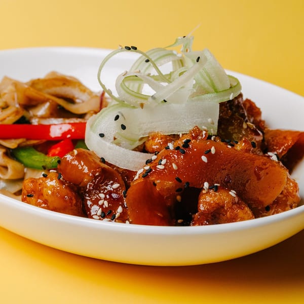 Sweet and sour chicken with noodles, red peppers, and green onions, garnished with sesame seeds.