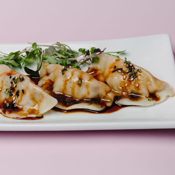 Three Asian-fusion dumplings drizzled with sauce and garnished with microgreens on a white plate.