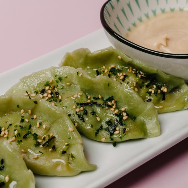 Green dumplings topped with sesame seeds and herbs, served with a creamy dipping sauce.