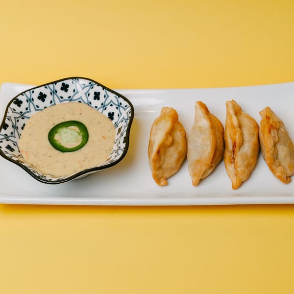 Four golden-fried dumplings and a patterned bowl of creamy sauce with a jalapeño slice on a white plate.
