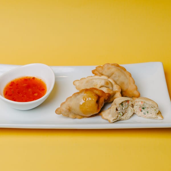 Fried dumplings with a sweet chili dipping sauce on a white rectangular plate against a yellow background.